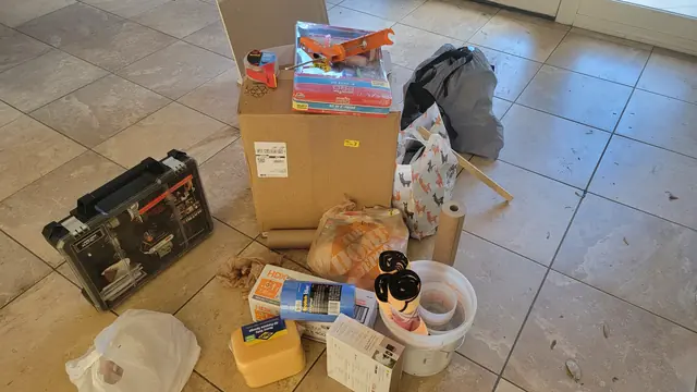 New painting and prep supplies staged on a tile floor, including roller kits, tape, sheeting and buckets