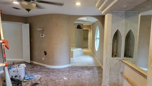 A bedroom mid-renovation with skim-coated walls and an arched opening to a bathroom