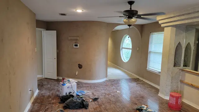 A room under renovation with stripped walls, a round leaded-glass window and sanding tools on the floor