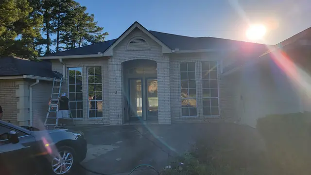 The front of a brick home at sunset with a worker on a multi-position ladder near the roofline