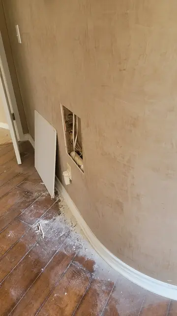 A wall opened up to expose wood framing and electrical wiring during an in-wall repair