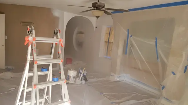 An interior room fully masked with plastic sheeting, with a ladder and airless paint sprayer staged