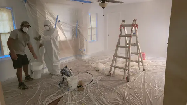 Two Handyman Saver crew members masking walls and spraying during a full interior repaint