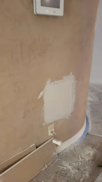 A fresh joint-compound drywall patch drying on a wall below a thermostat