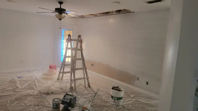 A room with freshly primed white walls, a ladder, primer cans and an airless sprayer on protected floors