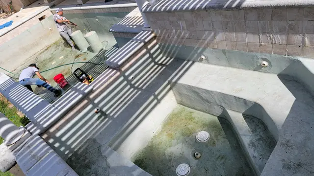 Two crew members pressure washing the plaster of a drained in-ground pool and spa