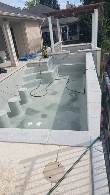 A drained in-ground pool with plaster partially cleaned, pressure washer on the steps