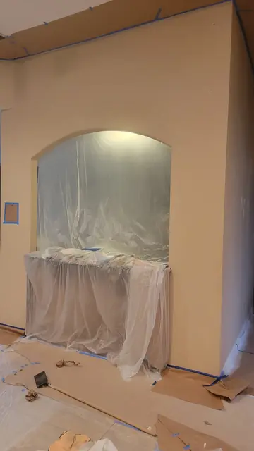 A freshly painted wall with an arched niche, fixtures wrapped in protective plastic sheeting